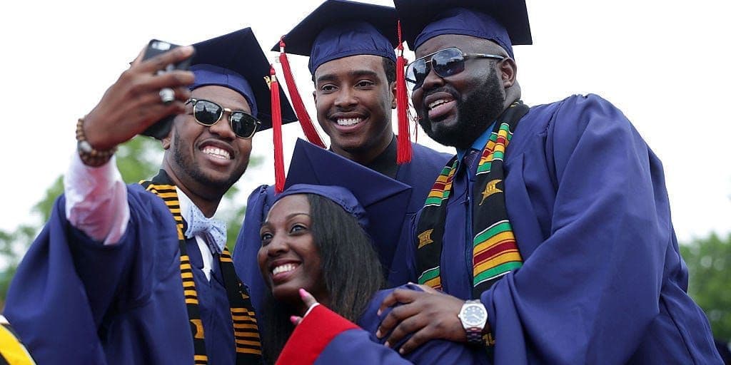 Graduates in gowns and kente stoles celebrating with a group selfie